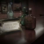 "Please Be Seated" sign and vintage bottles inside the Speakeasy escape room at Escape It Grandview in Columbus Ohio